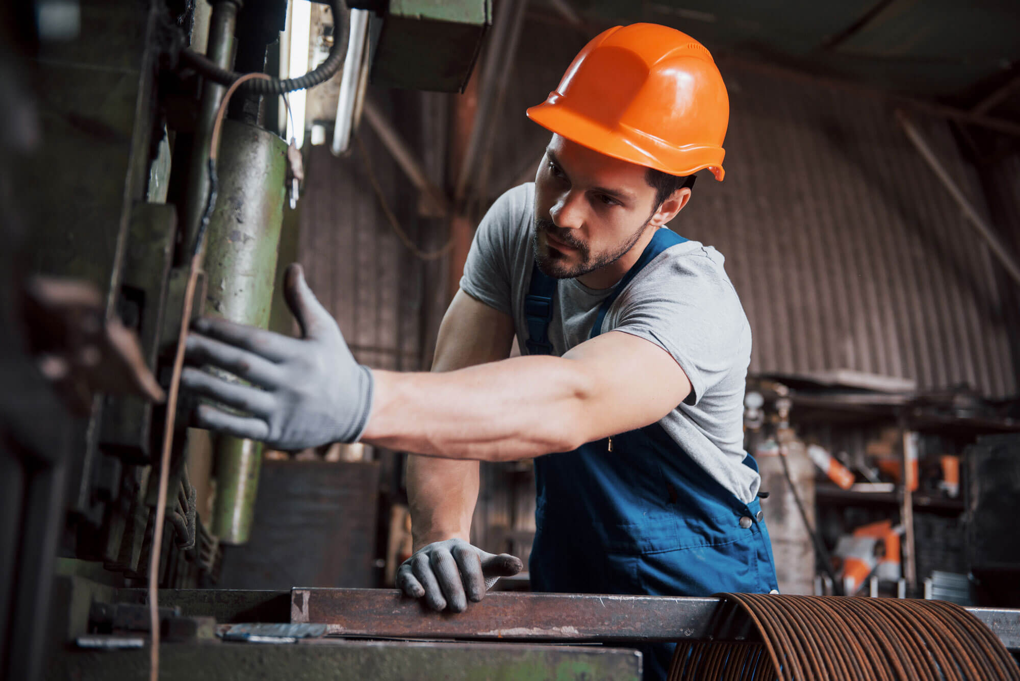 Un ouvrier portant un casque orange travaillant sur une machine dans une usine. Trouvez des missions industrielles avec Fusion Intérim Limoges.